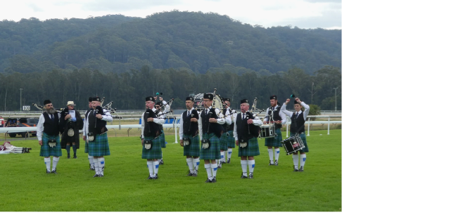 Pipers and drummers playing on a grassy field with the mountains behind them